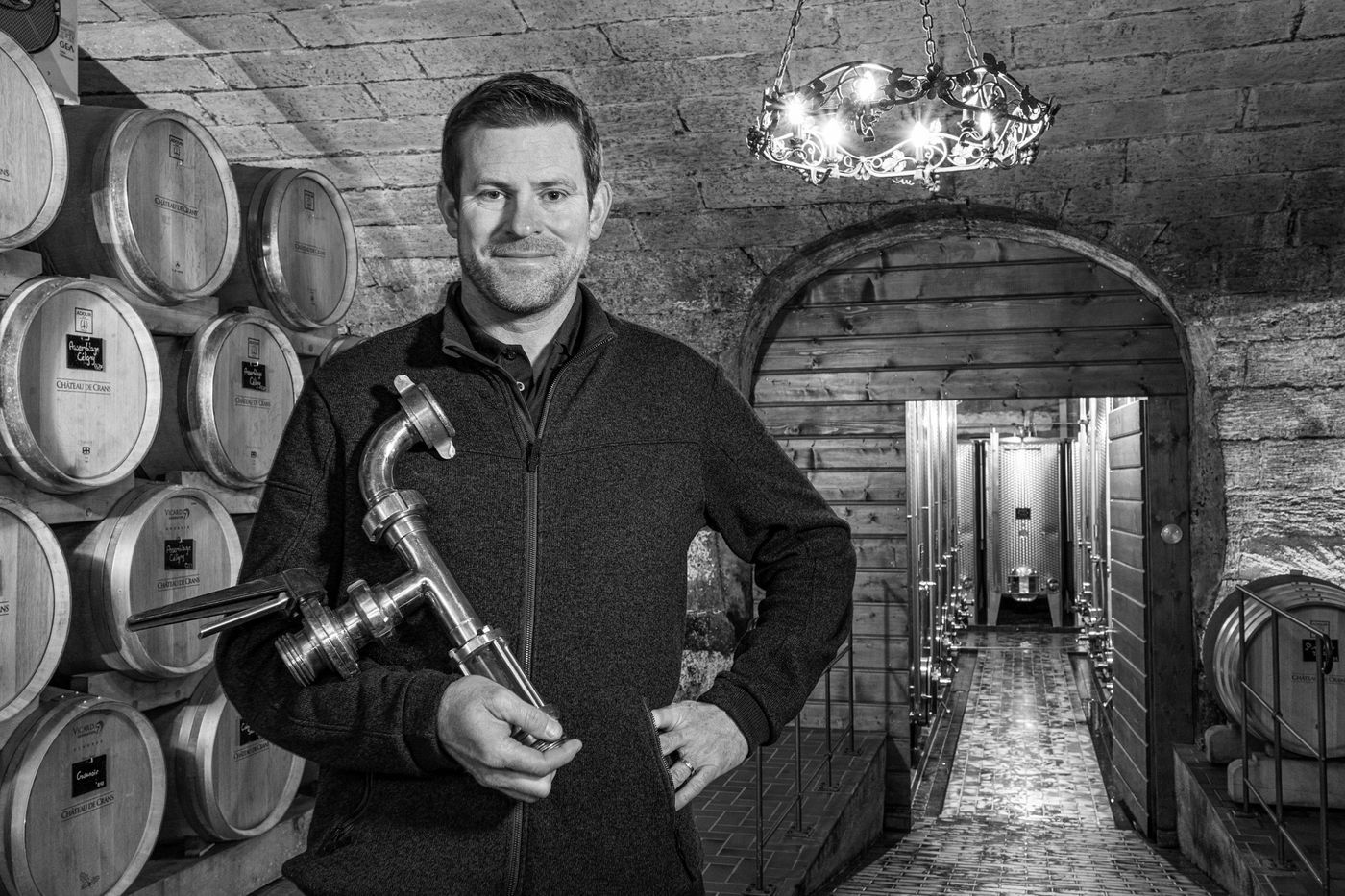 Portrait de Gilles Pilloud dans la cave du Château de Crans, entouré de barriques, illustrant le travail du vin et la signature du domaine.